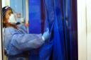 A nurse wearing full PPE adjusts a curtain on a ward for Covid patients