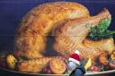 A shopper, wearing a protective facemask and Santa hat, passes a billboard poster featuring a Christmas turkey.