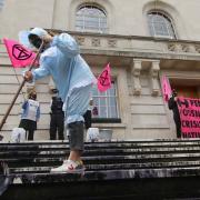 A climate protester dressed in baby garb smears a black oily substance on the steps of Hackney Town Hall.