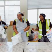 Volunteers Ziggy Noonan, Carletta Gorden, and Michelle Dornelly sing along to Whitney Houston as they pack bags with food at the Community Food Hub in the Wilton Estate Community Centre, April 6, 2020. Michelle started Children With Voices 25 years ago,